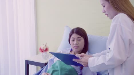 Beautiful-smart-Asian-doctor-and-patient-discussing-and-explaining-something-with-clipboard-in-doctor-hands-while-staying-on-Patient's-bed-at-hospital.-Medicine-and-health-care-concept.