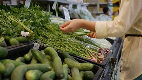 Manos-de-mujer-elige-hojas-de-cebolla-en-el-supermercado.-Mujer-joven-comprando-comida-sana-en-el-fondo-de-desenfoque-de-una-tienda