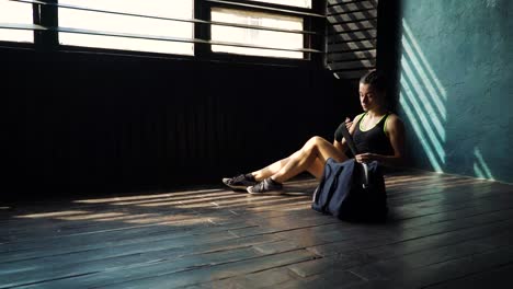 Panning-young-beautiful-woman-sitting-on-floor-and-wrapping-hands-with-black-boxing-wraps-in-club.