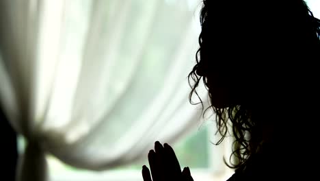 Female-in-silhouette-bows-talking-with-God-in-prayer,-hands-folded,-indoors