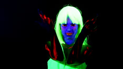 Woman-with-UV-face-paint,-wig,-glowing-clothing-dancing-in-front-of-camera,-shoulder-shot.-Caucasian-woman.-.