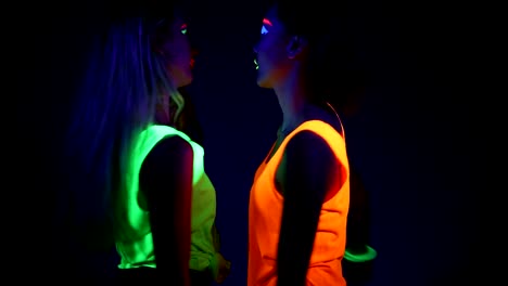 Women-with-UV-face-paint,-laser,-glowing-bracelets,-glowing-clothing-dancing-together-in-front-of-camera,-Half-body-shot.-Caucasian-and-asian-woman.-.