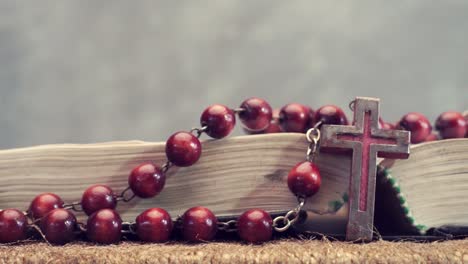 Open-Bible-and-the-crucifix-beads-on-a-golden-table,-close-up.-Beautiful-dark-background.-Religion-concept