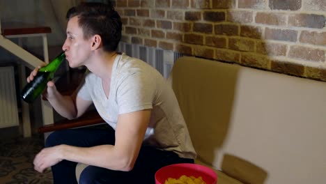 Man-drinks-beer-and-chips-in-front-of-TV-watching-football