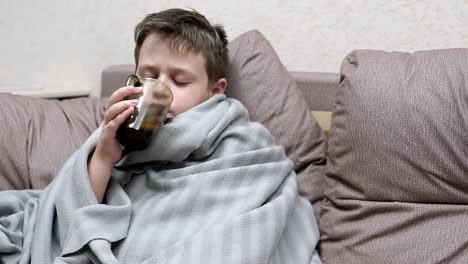 The-boy-drinks-medicine-and-tea-with-lemon.-He's-got-a-cold