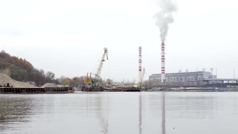 El-puerto-industrial-vierte-arena-en-la-barcaza-con-una-grúa.-En-el-fondo---planta-termosolar