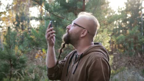 Ein-junger-Mann-mit-einem-Bart-schwört-und-schreit-auf-dem-Handy-gegen-den-herbstlichen-Wald