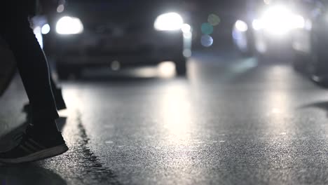 Pedestrians-feet-crossing-street-at-night-at-120fps-slow-motion.-Car-lens-flares-in-the-background-while-commuters-appear-in-the-foreground