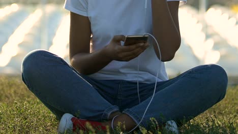 Woman-sitting-in-yoga-position-on-grass-and-listening-to-music-on-smart-phone