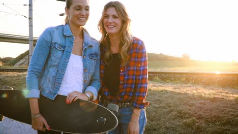 zwei-schöne-und-junge-Frauen-gehen-und-sprechen-mit-skateboard