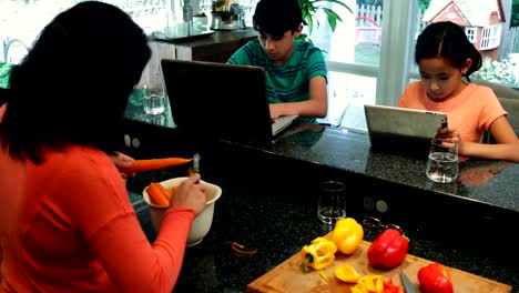 Kids-using-laptop-and-digital-tablet-while-mother-cutting-vegetables-4k