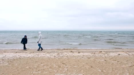 Mom-and-son-are-walking-on-the-sea-sand-beach-in-winter,-back-view.