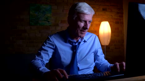 Closeup-portrait-of-old-caucasian-businessman-playing-video-games-on-the-computer-indoors-in-the-apartment-with-lights-off