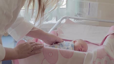 Mother-covering-sleeping-newborn-baby-with-blanket-in-maternity-hospital