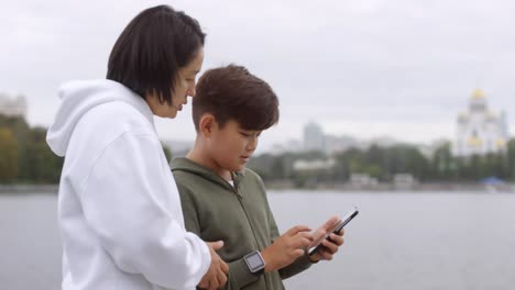 Madre-asiática-e-hijo-usando-Smartphone-antes-del-entrenamiento-al-aire-libre