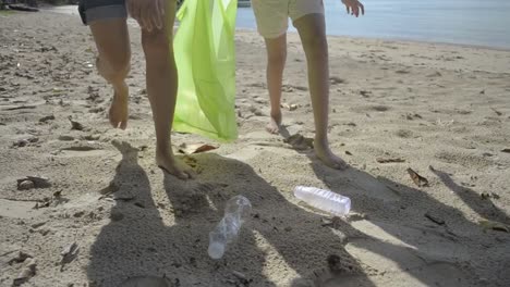 Mamá-y-su-hija-recogiendo-basura-en-la-playa-de-arena-en-una-bolsa-de-plástico-verde,-las-botellas-de-plástico-se-recogen-en-la-playa,-los-voluntarios-limpiando-la-playa.