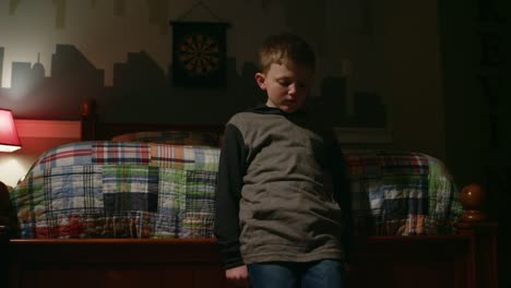 Sad-young-boy-stands-at-the-foot-of-his-bed,-crosses-his-arms