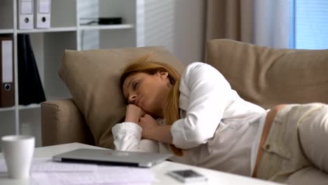 Tired-businesswoman-sleeping-on-the-couch-in-the-office-with-laptop-on-her-lap