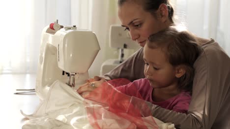 Joven-atractiva-madre-trabajando-en-la-máquina-de-coser-con-su-hija-poco-Linda