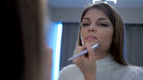 Young-Woman-Putting-Make-Up-on-Face-in-Mirror