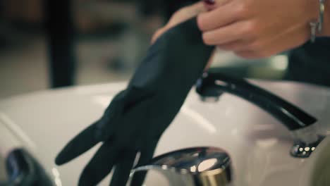 Woman-gently-pulls-black-rubber-gloves-on-her-hands-above-sink.-Closeup.-Slow-mo