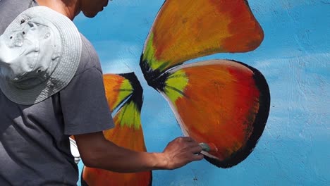 Pintor-mural-pinta-mariposa-en-color-en-la-pared-de-la-escuela.