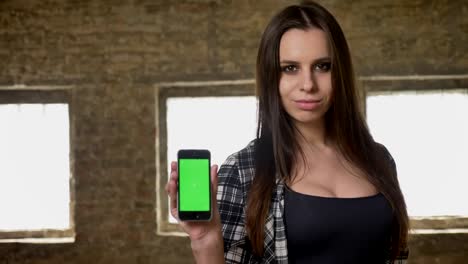 Young-beautiful-attractive-women-with-long-hair-showing-something-on-her-phone,-green-screen-on-phone's-display-and-nodding,-brick-building-background