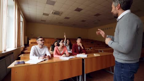 Professor-is-asking-question-and-pointing-at-students-waiting-for-answer,-young-people-are-raising-hands-and-speaking.-Checking-knowledge-and-teaching-concept.