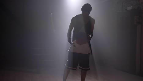 One-basketball-player-playing-with-ball-in-misty-dark-room-with-floodlight