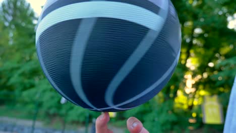 Man's-hand-balancing-and-spinning-basketball-on-finger-in-open-area,-park-in-background