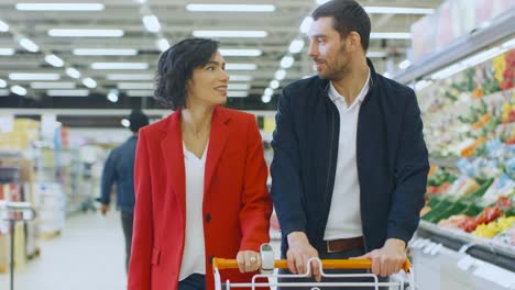 En-el-supermercado:-joven-pareja-camina-a-través-de-la-sección-de-productos-frescos-de-la-tienda-feliz,-hablar,-hombre-mujer-abraza-amorosamente.