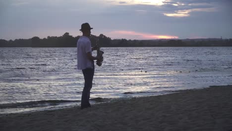 Handsome-young-guy-is-playing-the-saxophone-on-the-river-bank