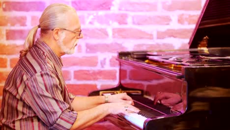 Man-musician-playing-the-piano.-He's-wearing-a-plaid-shirt,-glasses,-a-gold-watch,-rings.-Gray-hair