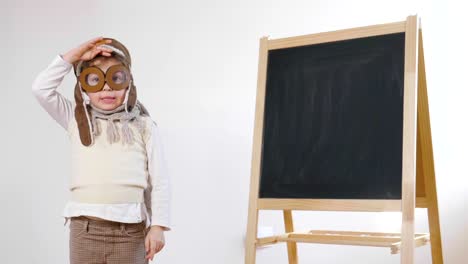 A-little-girl-dressed-as-an-airman-or-a-pilot,-indicates-with-her-hand-the-blackboard-behind-her-as-a-flight-insign-to-learn-to-use-both-aircraft-and-imagination.