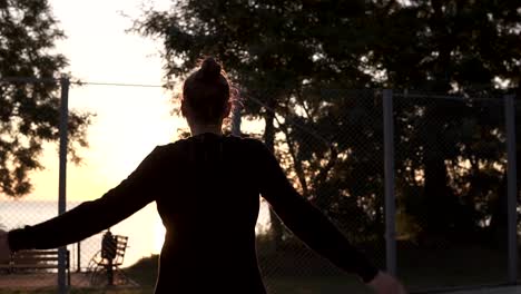 Caucasian-young-fit-woman-in-hoodie-warming-up-in-morning-on-basketball-court.-Stretching-her-legs-and-hands-before-basketball-training.-Backside-footage