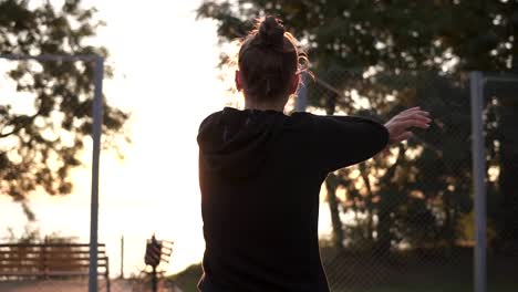 Caucasian-young-woman-warming-up-in-morning-on-basketball-court.-Stretching-her-arms-before-basketball-training.-Backside-footage