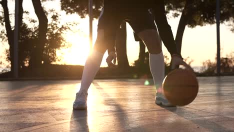 Imágenes-de-una-piernas-de-atleta-femenina-en-golf-blanco-calcetines-y-zapatillas-de-deporte-de-cerca.-Reproductor-femenino-baasketball-bola-que-despide-de-mano-a-mano.,-practicando-ejercicio-de-piernas-cruzadas.-Sol-brilla-en-el-fondo