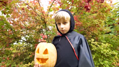 Boy-in-Halloween-costume-holding-pumpkin-jack-o-lantern,-alone-in-forest,-spooky