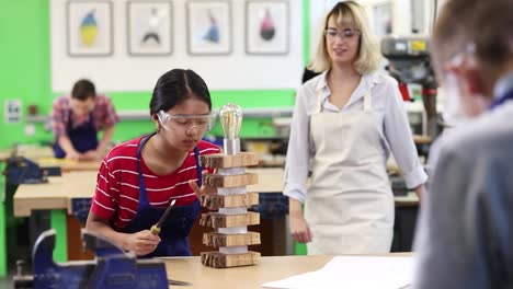 Teacher-Helping-Female-High-School-Student-Building-Lamp-In-Woodwork-Lesson