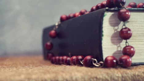 Open-Bible-and-the-crucifix-beads-on-a-golden-table,-close-up.-Beautiful-dark-background.-Religion-concept