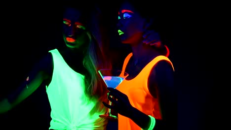 Women-with-UV-face-paint,-laser,-glowing-bracelets,-drinks,-glowing-clothing-dancing-together-in-front-of-camera,-Half-body-shot.-Caucasian-and-asian-woman.-.