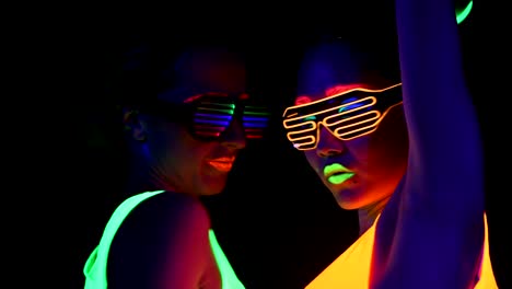 Women-with-UV-face-paint,-glowing-clothing,-glowing-bracelet,-glasses-dancing-in-front-of-camera,-face-shot.-Caucasian-and-woman.-.