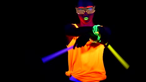 Woman-with-UV-face-paint,-glowing-clothing,-glowing-glasses,-bracelet-dancing-in-front-of-camera-holding-chemical-light,-half-body-shot.-Asian-woman.-.