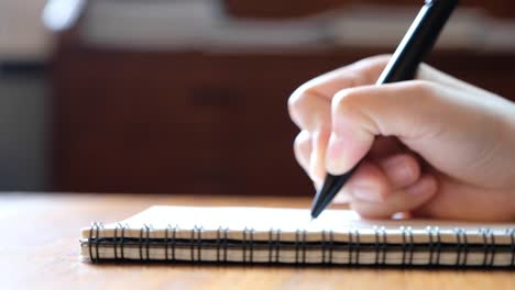 a-woman's-hand-writing-on-blank-notebooks-on-wooden-table