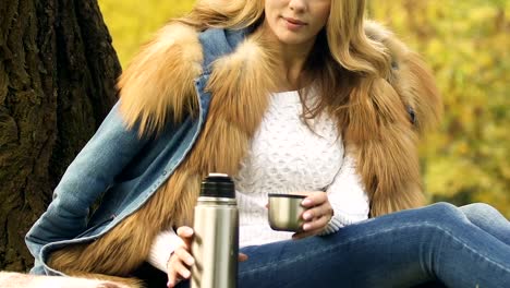 Girl-pouring-tea-from-thermos,-enjoying-hot-drink-in-autumn-forest,-comfort