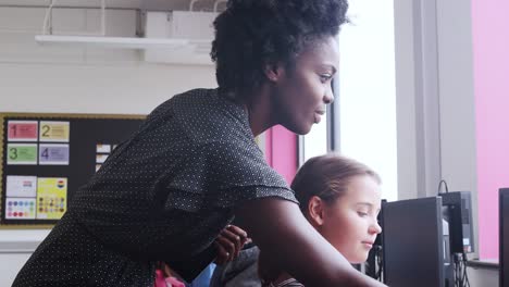 Teacher-Helping-Female-Pupil-In-Line-Of-High-School-Students-Working-at-Screens-In-Computer-Class