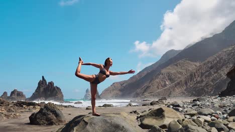 hübsche-blondes-Mädchen-in-schwarzen-Top-entspannt-sich-in-Yoga-Pose-Lotus-auf-lila-Matte-gegen-die-Wellen-des-Ozeans,-die-auf-Felsen