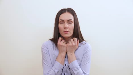 A-brown-haired-woman-is-looking-into-the-camera-holding-hands-pressed-to-chest,-palm-under-the-chin.-She-opens-and-shuts-the-fists,-puts-hands-down.