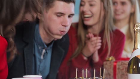 Handsome-man-blowing-birthday-candles-while-close-friends-throwing-a-surprise-party,-slowmotion-in-cozy-modern-apartment