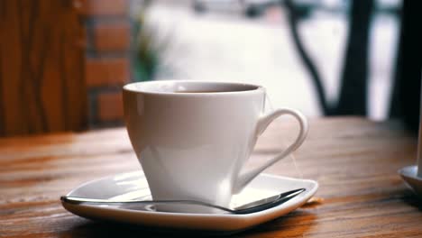 White-Cup-of-Hot-Tea-on-the-Table-in-a-Cafe-on-the-Background-of-the-Street-Window